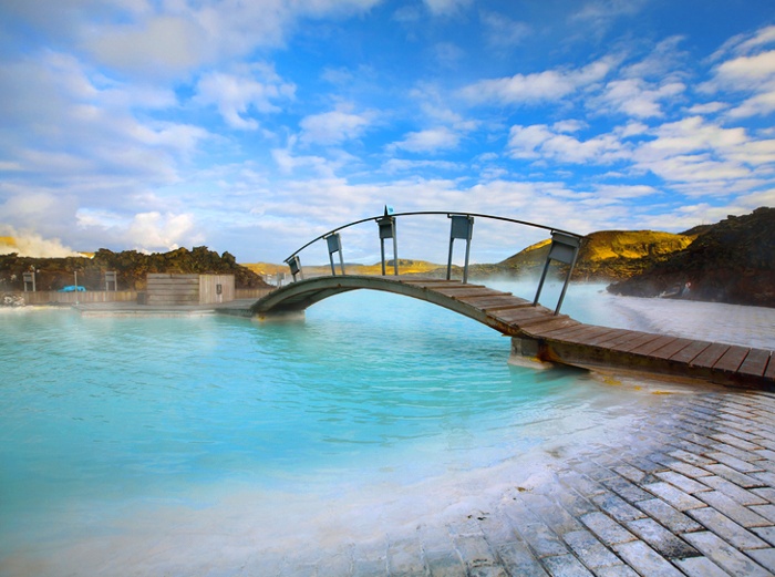 Scenic view of a bridge at the Blue Lagoon in Iceland, showcasing serene blue geothermal waters surrounded by rocky volcanic landscape and steam rising from the lagoon.