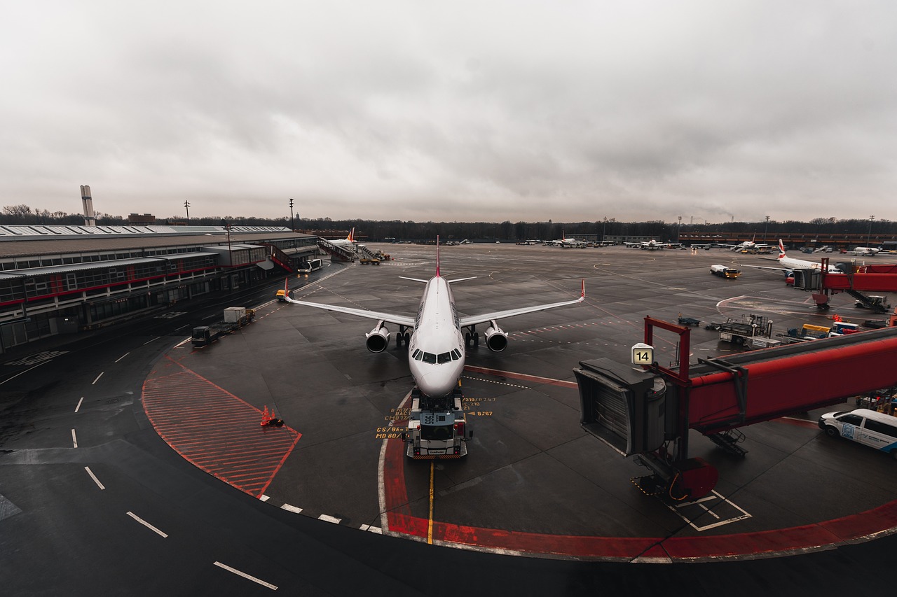 Commercial airplane waiting on the tarmac, ready for departure, with a blurred background of airport buildings and vehicles.