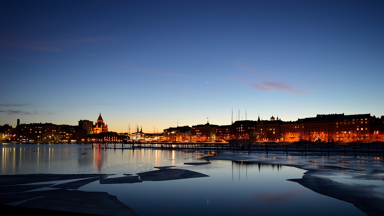 Helsinki, Finland harbour at sunset: sailboats and city skyline reflected in calm waters.