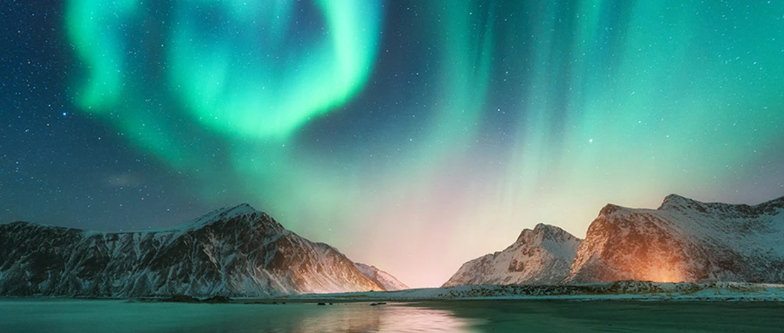 Spectacular Northern Lights illuminating the night sky with vibrant greens and purples, reflected beautifully on the calm, dark waters below, surrounded by a tranquil and icy landscape.