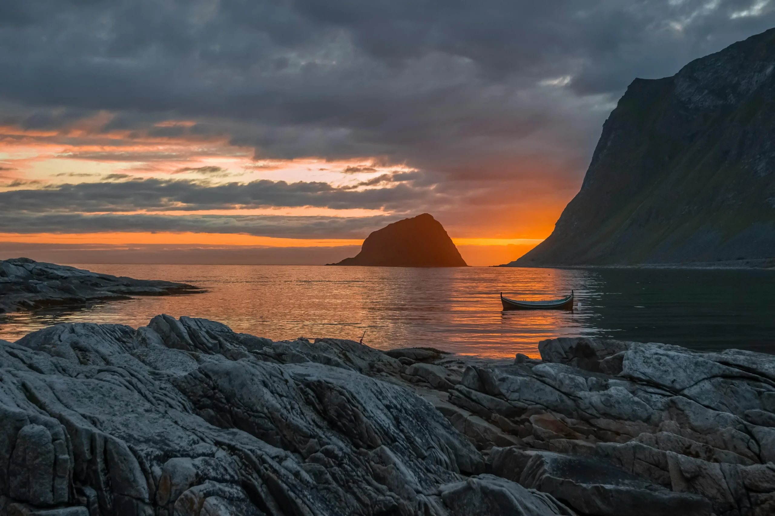 A serene and idyllic view of Haukland Beach in Norway, featuring white sand, crystal-clear turquoise water, and majestic mountains rising in the background.